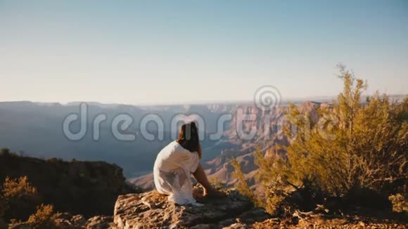 镜头在宁静的年轻女子上方坐在史诗般的日落全景中展现雄伟的大峡谷天际线视频的预览图