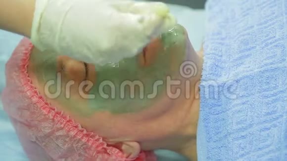 一位女性美容师用一个治愈泥面具涂在一个男人的脸上用刷子视频的预览图