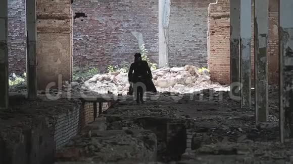 一个穿着雨衣和帽子的大胡子男人穿过一个废弃的工厂跳过地板上的大坑视频的预览图