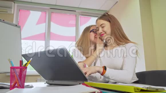 十几岁的女孩在学校用笔记本电脑工作时窃窃私语视频的预览图
