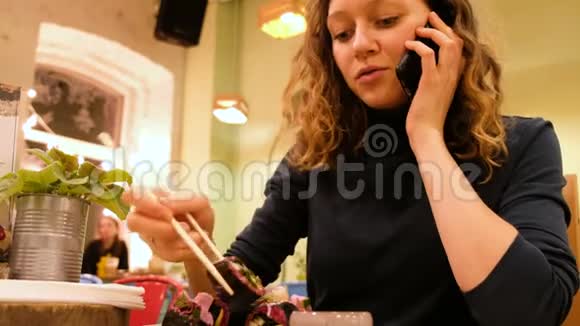 在素食咖啡馆里一个迷人的女孩在打电话吃着生的食物卷视频的预览图