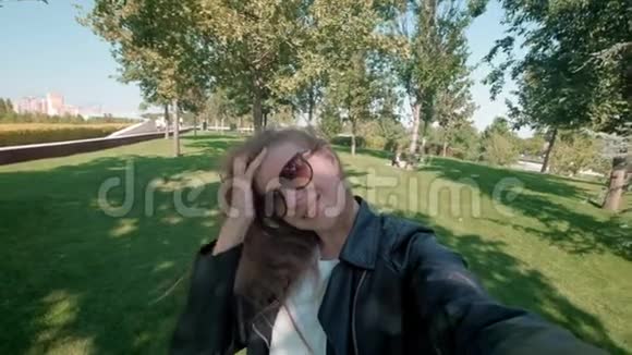 公园里的女学生穿着皮夹克的迷人女孩漫步在秋天公园在镜头前拍摄自己的照片视频的预览图