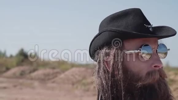 一个留着胡子和墨镜的硬汉正在沙漠中行走他脸上的特写视频的预览图