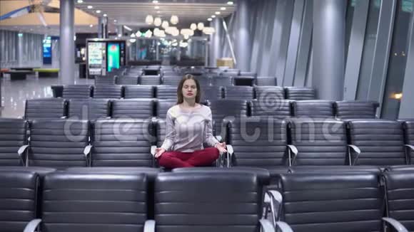 美丽的年轻休闲女子在空无一人的机场候机楼做瑜伽冥想视频的预览图