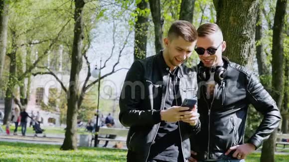 两个年轻人在公园里用电话听音乐耳机移动应用视频的预览图