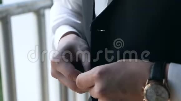 穿着西装和白色衬衫的时髦男人扣着一件背心背心站在窗户附近关门视频的预览图