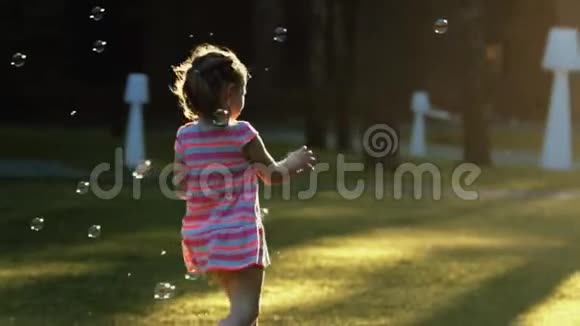 小美丽的女孩在日落时缓慢地捕捉泡泡视频的预览图