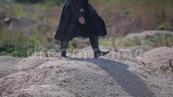 一个穿着黑色斗篷走过沙漠的神秘硬汉他的脚在干燥的岩石上视频的预览图