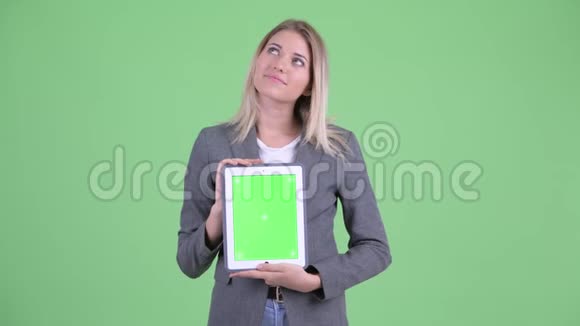年轻的金发碧眼的女商人一边思考一边展示数码平板电脑视频的预览图