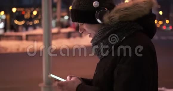 人们在寒冷的冬夜使用耳机和手机应用程序听音乐视频的预览图