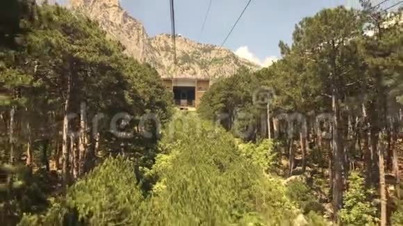 从窗口移动缆车舱在森林树木之间的山景在阳光明媚的天气里缆车在绳道上行驶视频的预览图