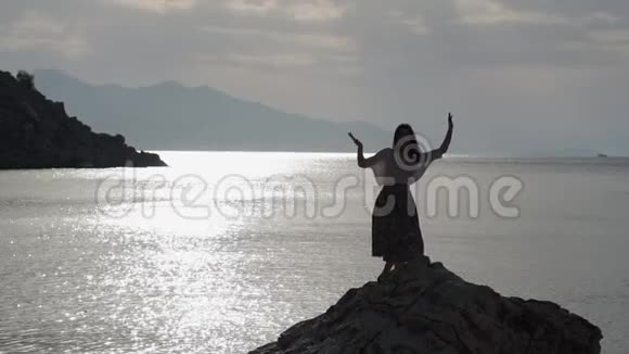 日落时分美丽的女人在海面上的岩石上缓慢地跳舞视频的预览图