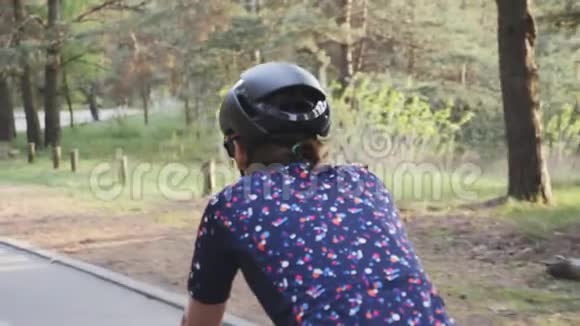在公园里穿着黑色头盔和蓝色球衣的女性骑自行车近距离拍摄慢动作视频的预览图