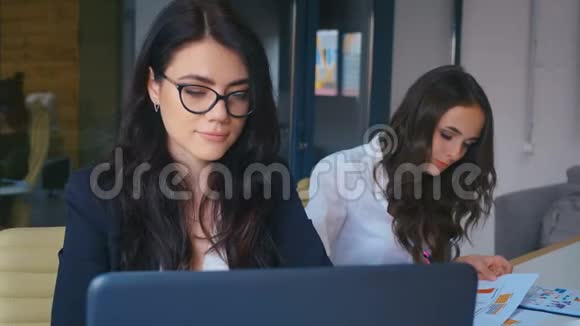 商务女性感到快乐微笑着看着办公室的镜头年轻女性在办公桌上使用笔记本电脑视频的预览图