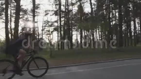 年轻漂亮的女孩骑自行车的部分跟随太阳穿过背景上的树木单车概念视频的预览图