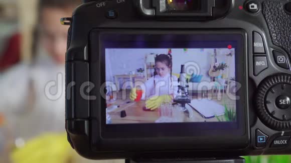 相机屏幕女孩青少年博客作者尤图伯穿着白色外套和护目镜在实验室家庭作业显微镜视频的预览图
