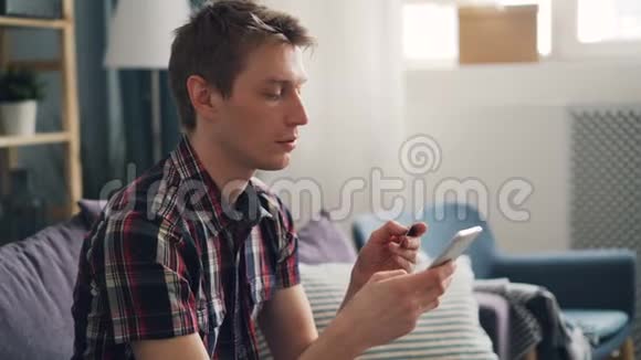 漂亮的男人正在用信用卡和智能手机触摸屏幕进行电子支付然后微笑着享受视频的预览图