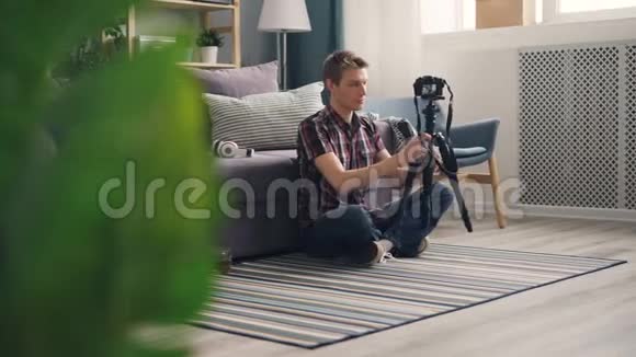 男性博主帅哥正在调整三脚架上的摄像头然后为坐在家里的在线博客录制视频视频的预览图