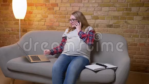 年轻孕妇在舒适的沙发上坐着一边用笔记本电脑一边打电话一边特写镜头视频的预览图