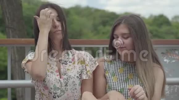 两个迷人的女孩坐在户外一起谈论新的指甲展示手指和指甲女朋友视频的预览图