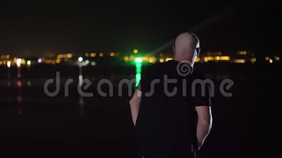 夜晚一个秃头正在跳舞从后面看在水面上发光的城市的灯光下视频的预览图