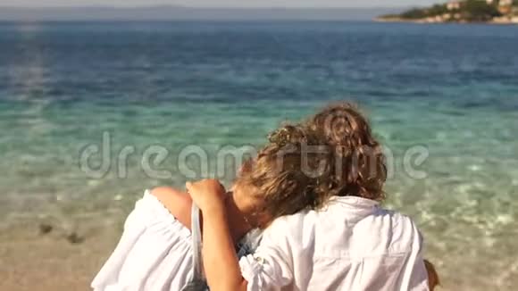 后景卷曲的男孩和女孩坐在最干净的绿松石海的岸边动态相机翻译视频的预览图