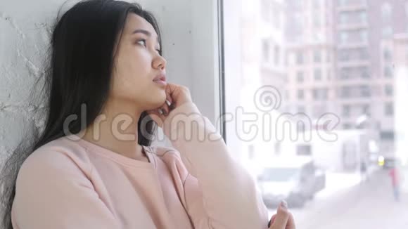 年轻的亚洲女人坐在窗前思考和思考视频的预览图