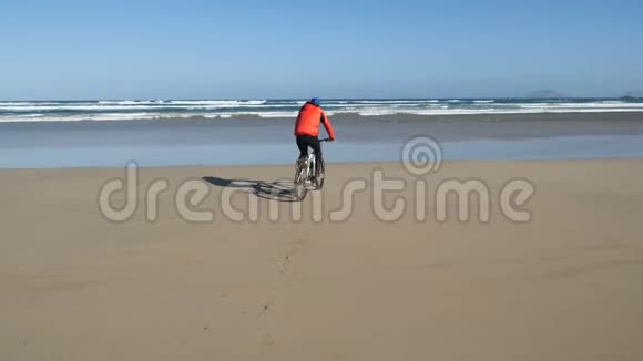 年轻人骑着自行车在加那利群岛的沙滩上朝大西洋的海浪走去兰萨罗特视频的预览图