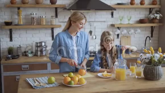 妈妈和女儿在厨房里做天然橙汁可爱的小女孩把桔子里的汁挤到罐子里视频的预览图