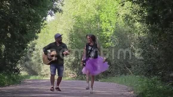 那个拿着吉他的家伙和他的女朋友在乡间小路上两个带吉他的情人旅行者漂亮的夫妇视频的预览图