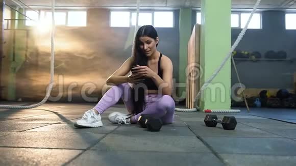 漂亮的女性在健身房训练后休息时使用智能手机视频的预览图