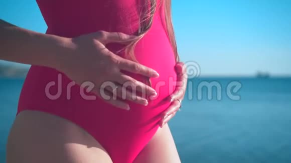 一个穿着红色一件泳衣的怀孕女孩站在海边抚摸她的肚子做得很好视频的预览图