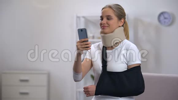 戴泡沫颈项圈和手臂吊带的开朗女人在手机康复中心聊天视频的预览图