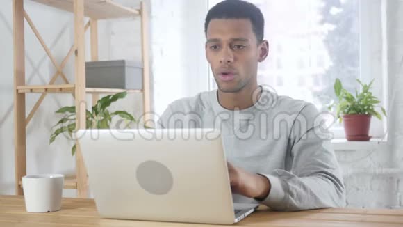 美国黑人男子坐在办公室因损失而烦恼工作在笔记本电脑上视频的预览图