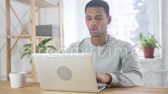 美国黑人男子坐在办公室因损失而烦恼工作在笔记本电脑上视频的预览图