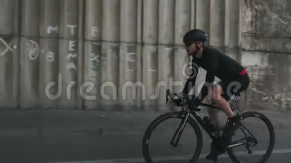 自信适合骑自行车的人骑自行车时戴着头盔黑色服装和太阳镜有胡子的自行车骑手骑自行车视频的预览图