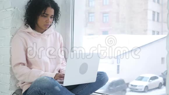 非洲裔美国妇女因损失而苦恼工作在笔记本电脑上坐在窗边视频的预览图