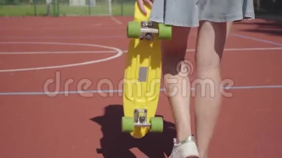 穿短裙的女人的腿和一个黄色的滑板在篮球场上行走影跟着女孩概念视频的预览图