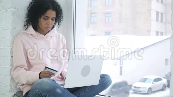 美国黑人妇女坐在窗边成功的网上购物视频的预览图