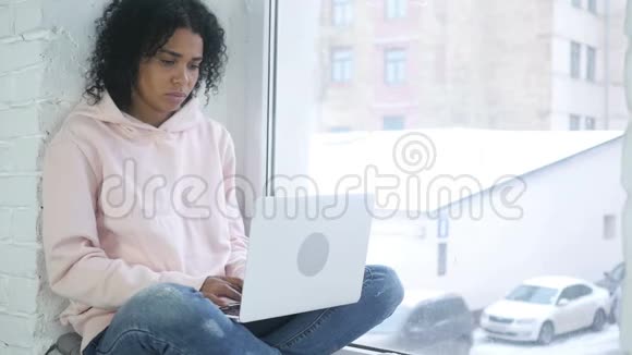 兴奋的非洲裔美国妇女庆祝成功工作在笔记本电脑上坐在窗口视频的预览图