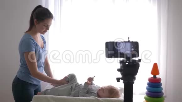 宝贝体操年轻的博主妈妈给小儿子做热身并用相机手机录制现场辅导视频视频的预览图