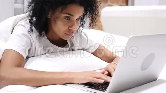 在笔记本电脑上工作的非裔美国妇女躺在床上休息视频的预览图