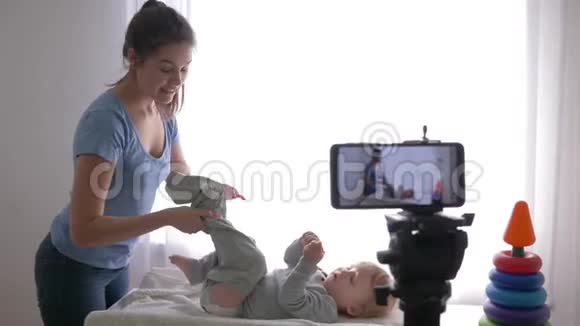 博客职业现代母亲vlogger在手机上录制训练视频时为小男孩换衣服视频的预览图