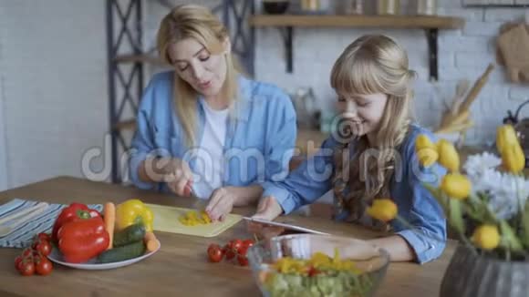 妈妈和女儿一起在厨房做饭看着网上的菜谱手机平板电脑4K视频的预览图