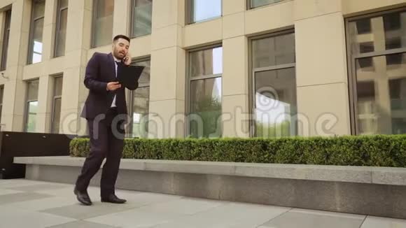 非常愤怒的商人拿着平板电脑走在街上用手机说话视频的预览图