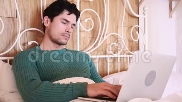 头痛疲劳的人在床上工作的笔记本电脑视频的预览图