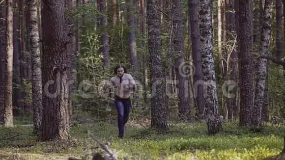 一个酷酷的家伙赤裸的躯干和一把刀在他的手中缓慢地向镜头穿过树林视频的预览图
