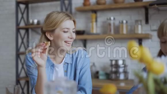 妈妈和女儿在厨房里笑喝橙汁和饼干和松饼可爱的快乐家庭对话视频的预览图