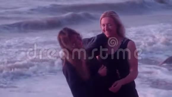 妈妈和女儿拥抱欢笑微笑在大海巨浪泡沫海滩的背景下视频的预览图