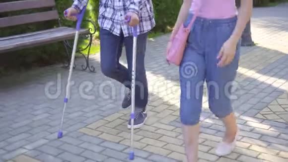 拄着拐杖断腿的亚洲青年男子与公园里的亚洲青年女子交流视频的预览图